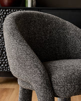 Easton dining chair in dark grey fabric, close-up of curved armrest and seat detail on wooden floor.