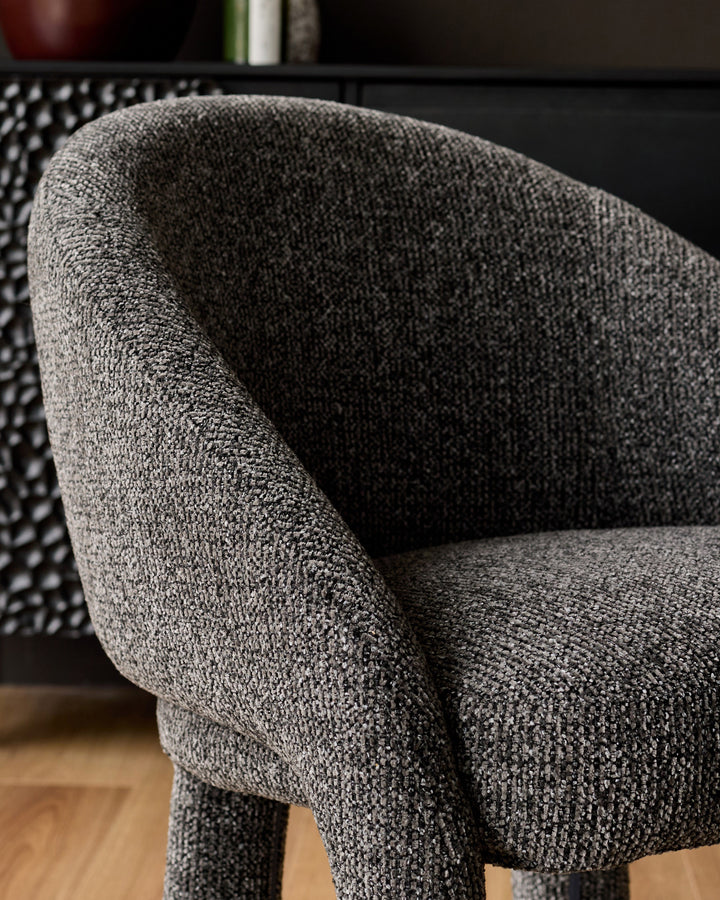 Easton dining chair in dark grey fabric, close-up of curved armrest and seat detail on wooden floor.