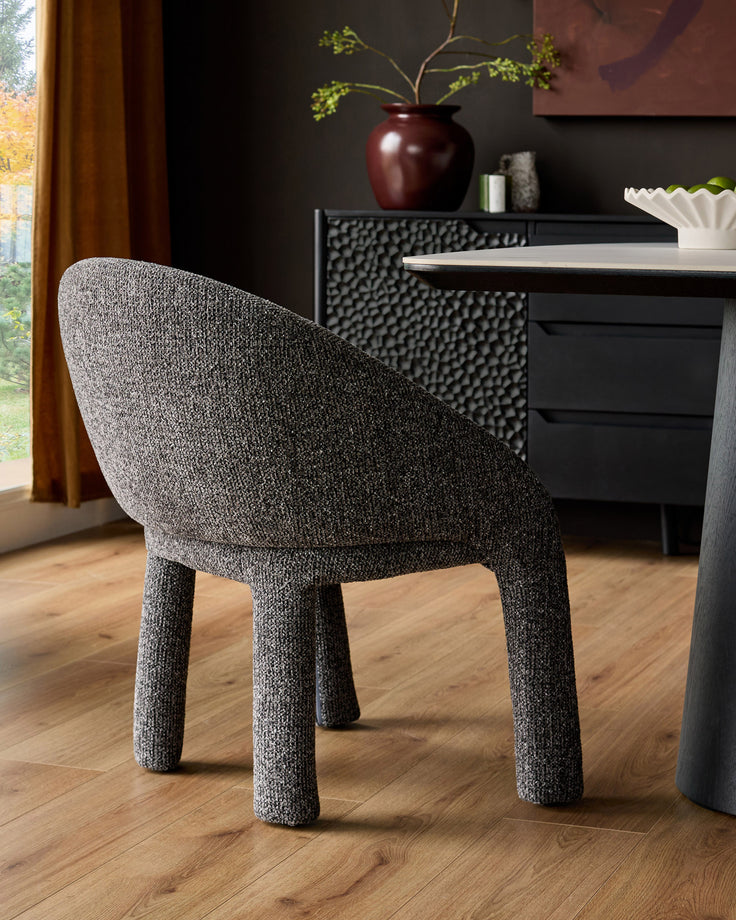Easton dining chair in dark grey fabric, shown from a rear three-quarter angle at a dining table in a modern interior setting.