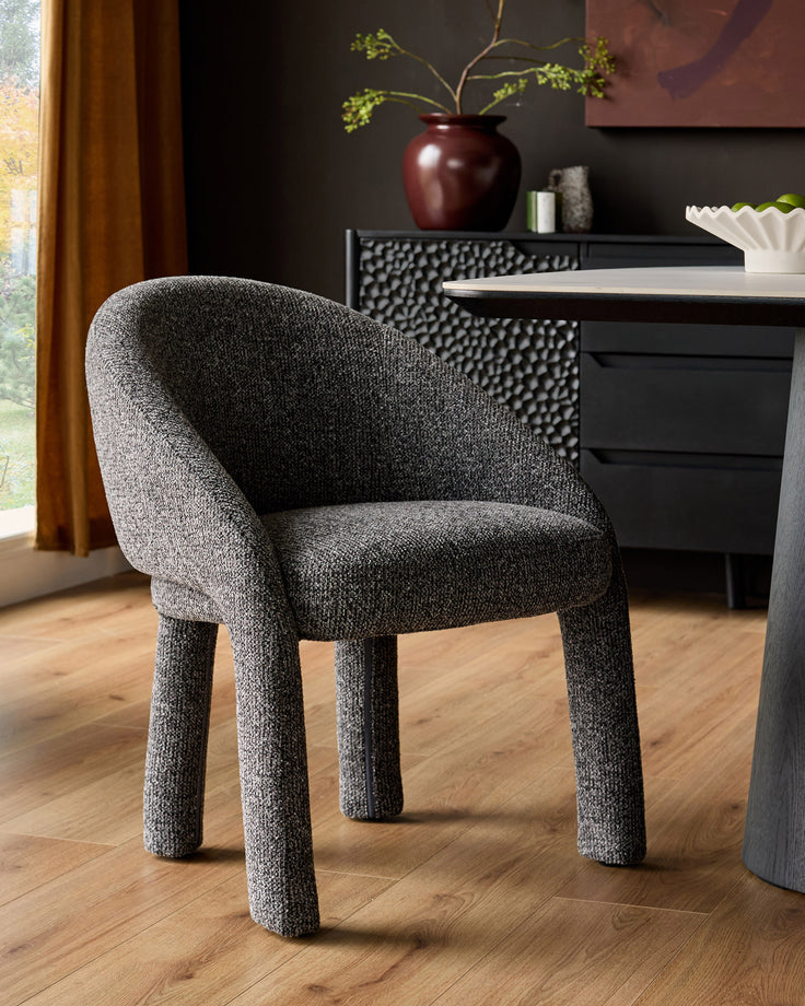 Easton dining chair in dark grey fabric with curved backrest and sturdy cylindrical legs, shown in modern interior setting.