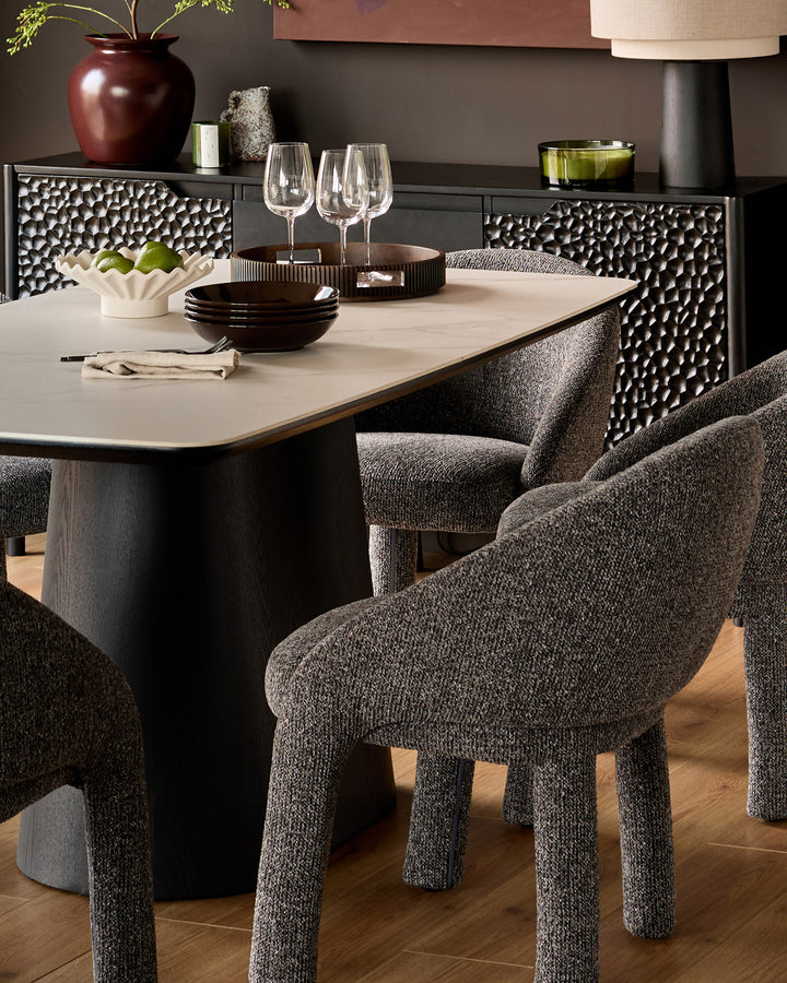Easton dining chair in dark grey fabric with rounded back and sturdy legs, shown at dining table.