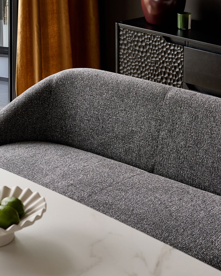Easton dining bench in dark grey fabric, curved backrest, white base, angled side view.