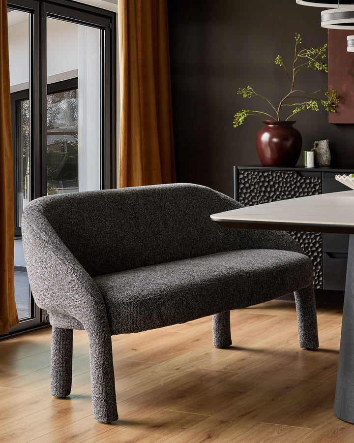 Dark grey fabric dining bench with curved backrest and cylindrical legs, shown in modern interior setting.