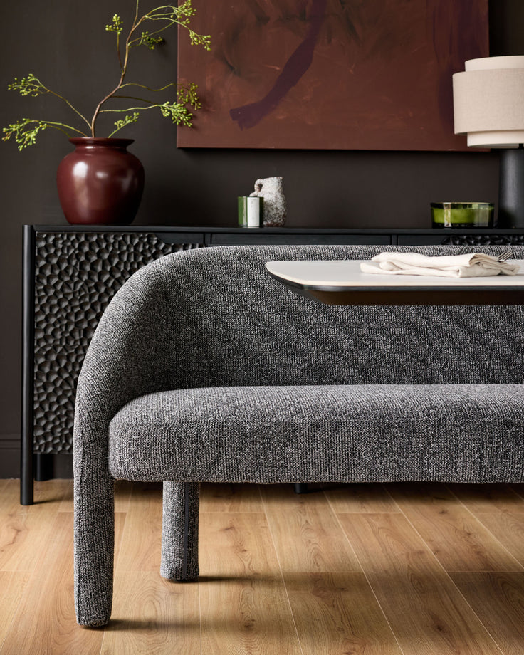 Easton dining bench in dark grey fabric with curved backrest, shown in modern room setting with wooden flooring.
