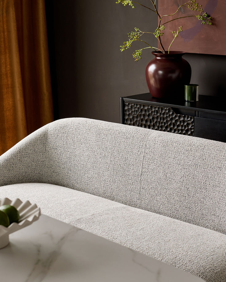 Easton dining bench in light grey fabric, curved backrest, shown in styled room setting with dark console table.
