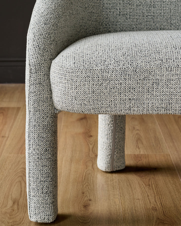 Easton dining bench in light grey fabric, showing curved armrest and cylindrical leg detail on wooden floor.