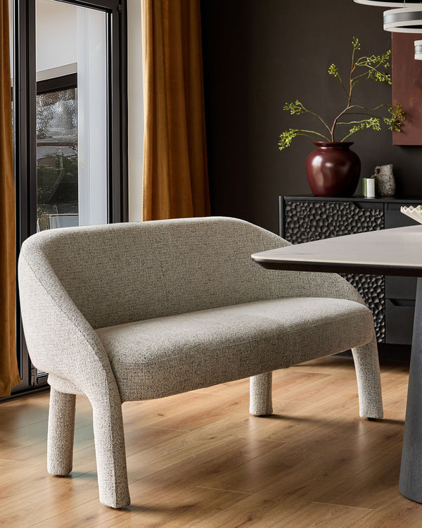Easton dining bench in light grey fabric with curved backrest and cylindrical legs, positioned at dining table.