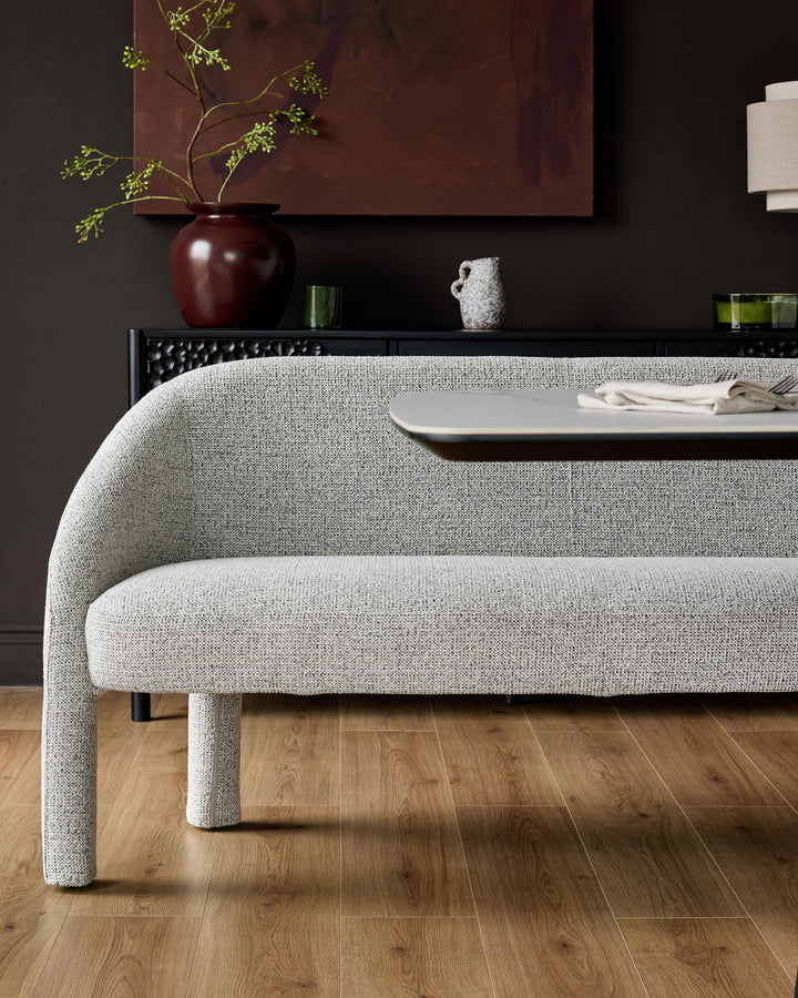 Easton dining bench in light grey fabric with curved backrest and legs, shown in a styled dining room setting.