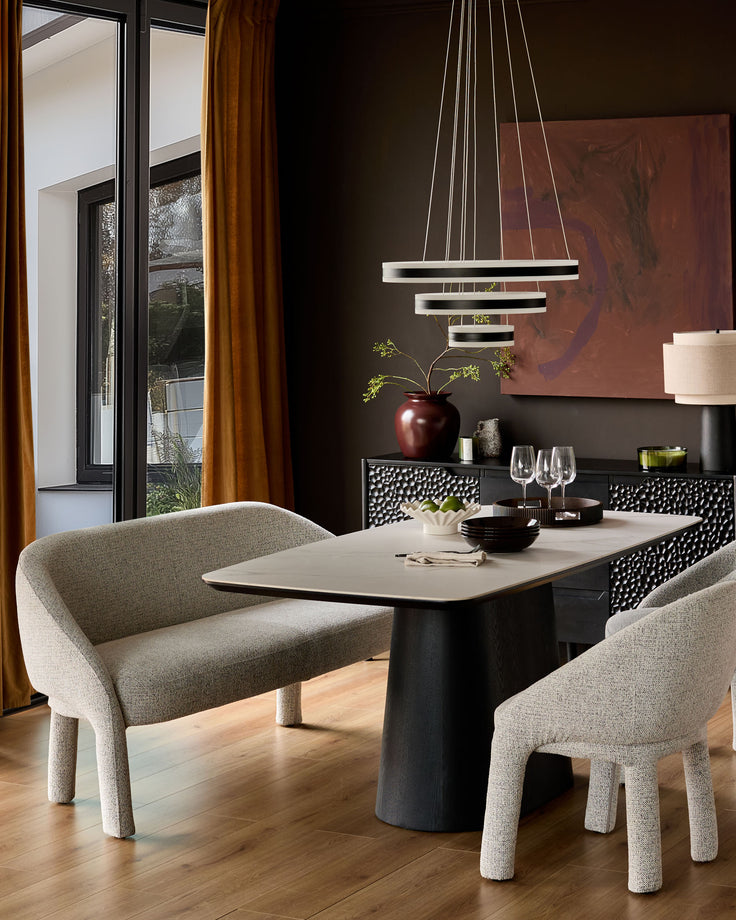 Easton dining bench in light grey fabric, curved backrest and rounded legs, positioned at dining table in modern room setting.