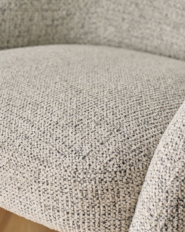 Close-up of light grey upholstered dining chair seat showing woven fabric texture and curved edge detail.
