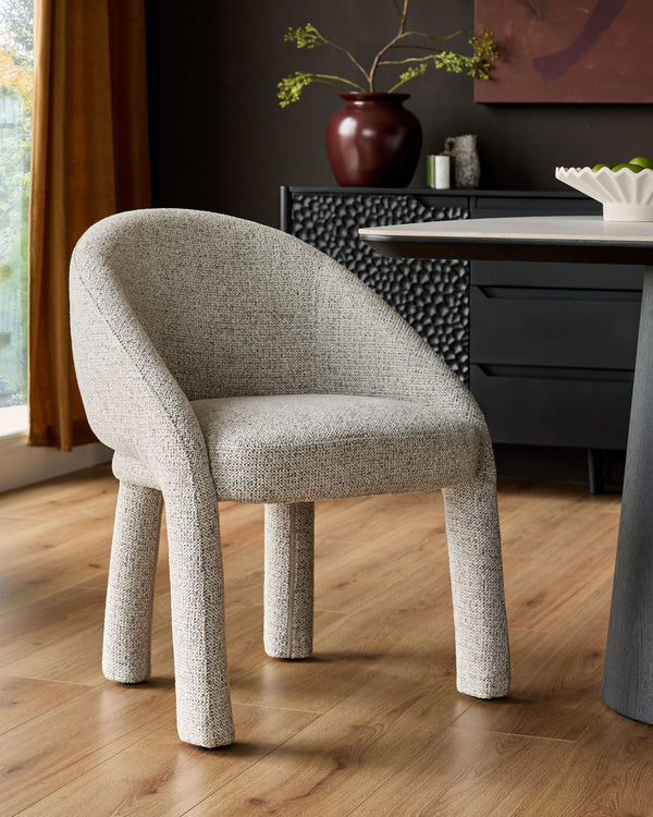Easton dining chair in light grey fabric with curved backrest and cylindrical legs, positioned at a desk in a modern interior.