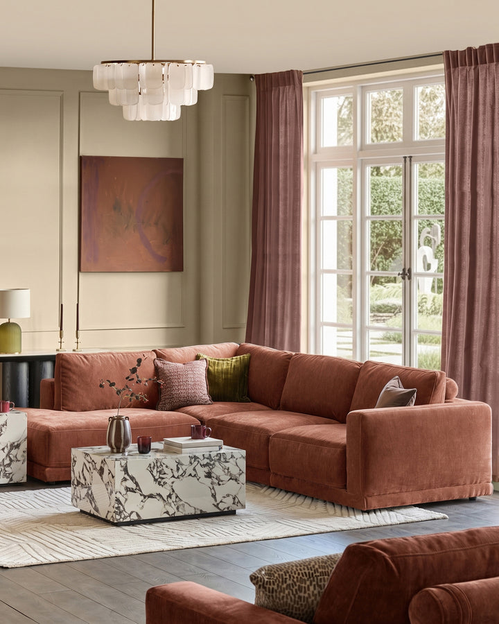 Eden Left Large Chaise Sofa in apricot fabric, displayed in a bright living room with marble coffee table and windows.