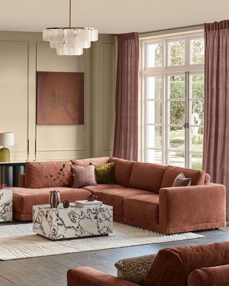 Eden Left Large Chaise Sofa in apricot fabric, displayed in a bright living room with marble coffee table and windows.
