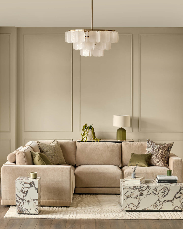 Estelle chandelier in white glass with brass finish, featuring tiered cylindrical shades in a modern living room setting.