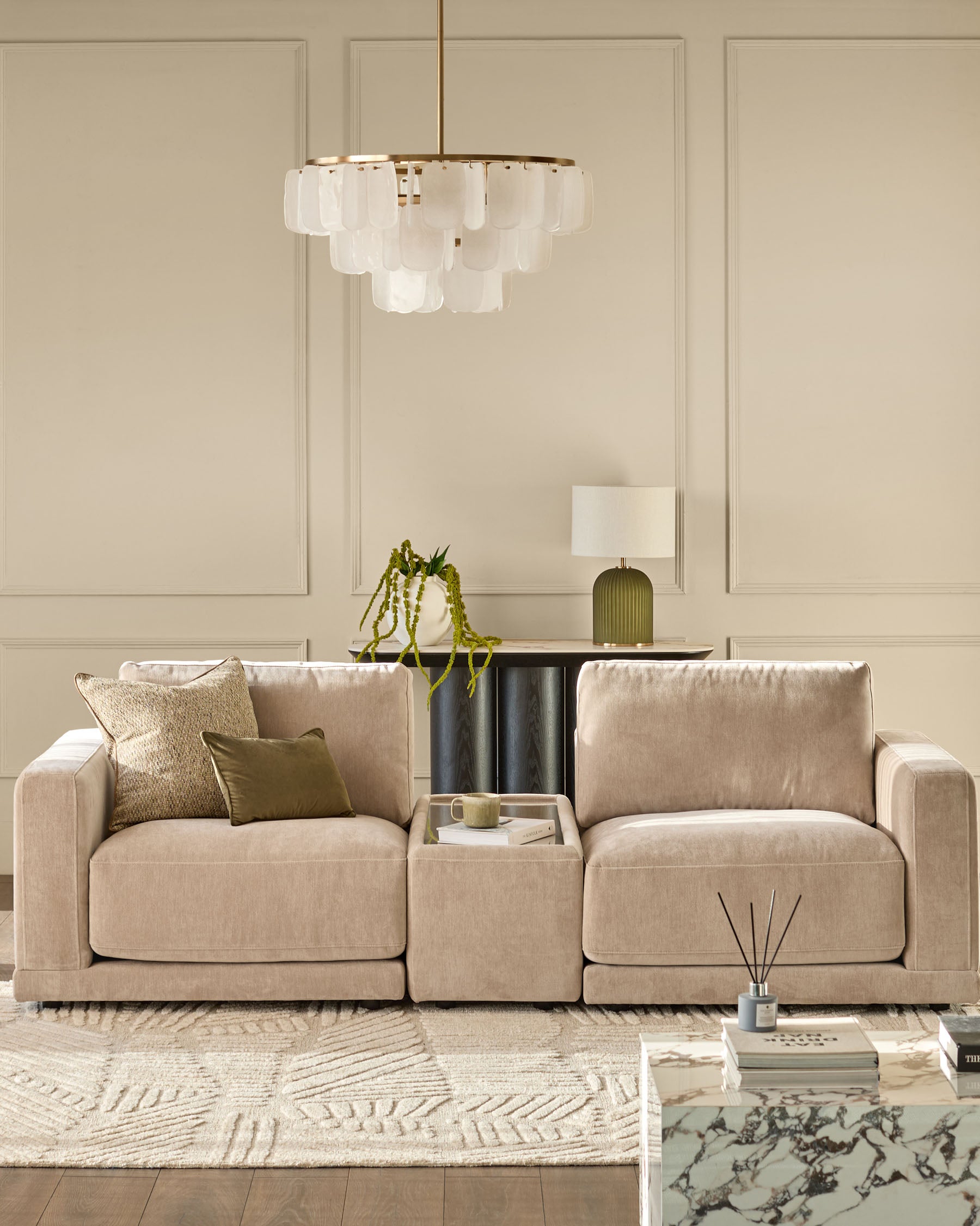 Champagne fabric side table module with glass top, shown between two beige sofas in a neutral living room setting.