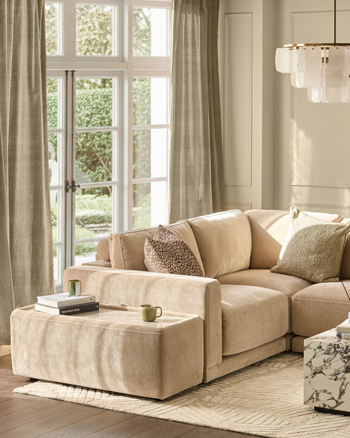 Champagne fabric side table module with glass top, positioned next to a beige sectional sofa in a bright living room setting.