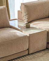 Eden side table module with glass top and champagne fabric base, positioned between two beige upholstered seating sections.