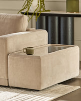Champagne fabric side table with open glass-top compartment, shown in living room setting next to beige sofa.