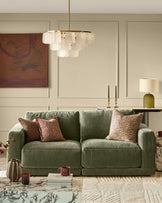 Estelle chandelier with white glass shades and brass finish, hanging in modern living room above green sofa.