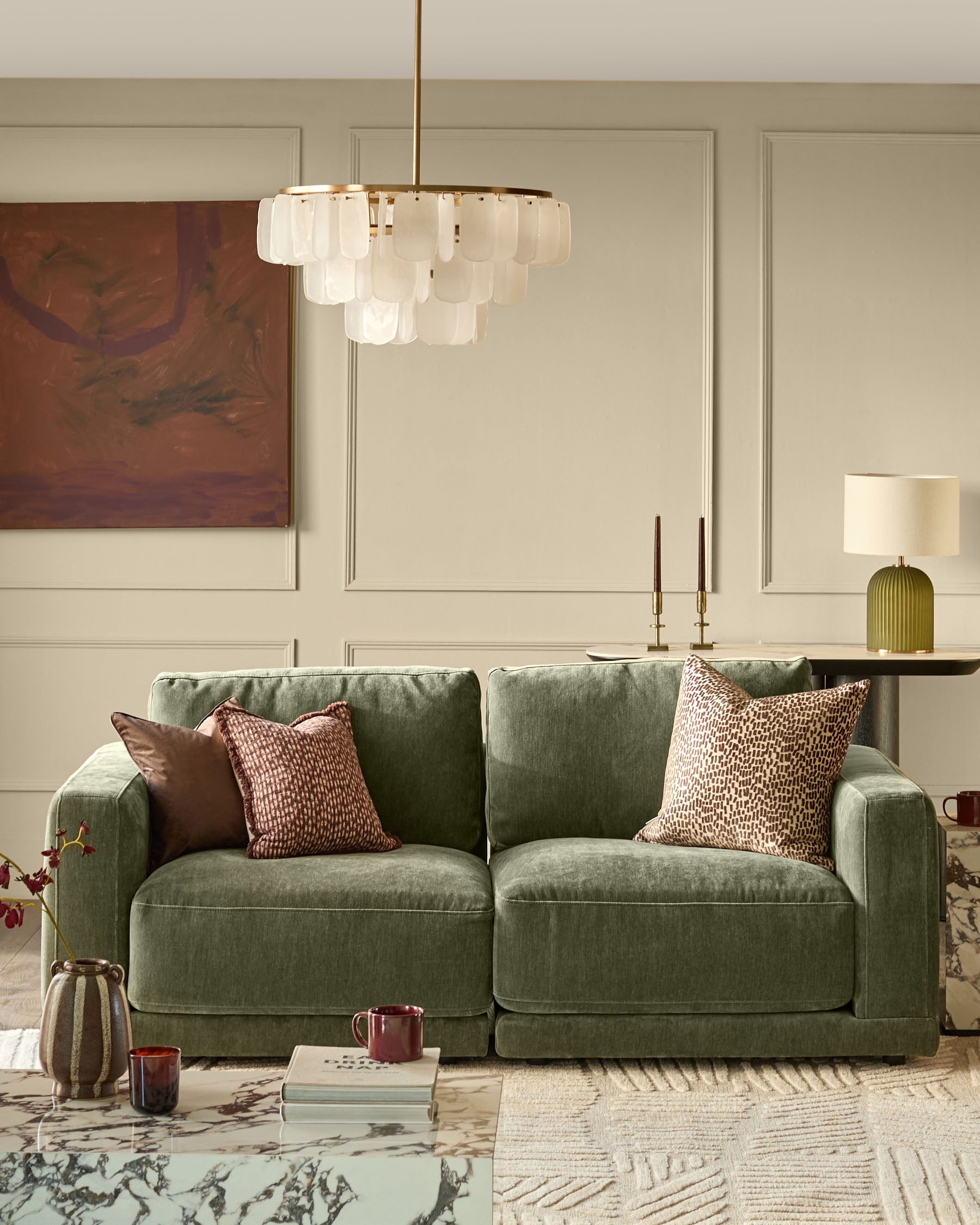 Estelle chandelier with white glass shades and brass finish, hanging in modern living room above green sofa.