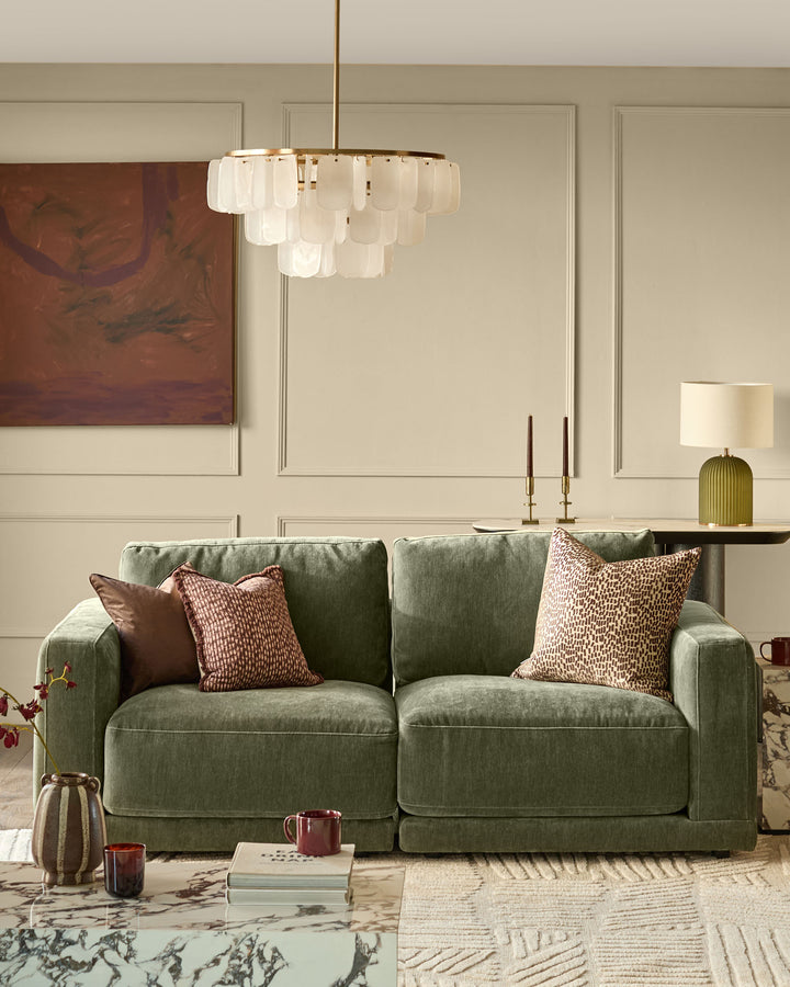 Estelle chandelier with white glass shades and brass finish, hanging in modern living room above green sofa.