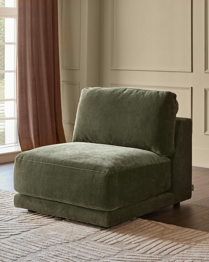 Eden single-module chair in dark green fabric, shown at an angle in a modern living room setting with neutral walls and burgundy curtains.