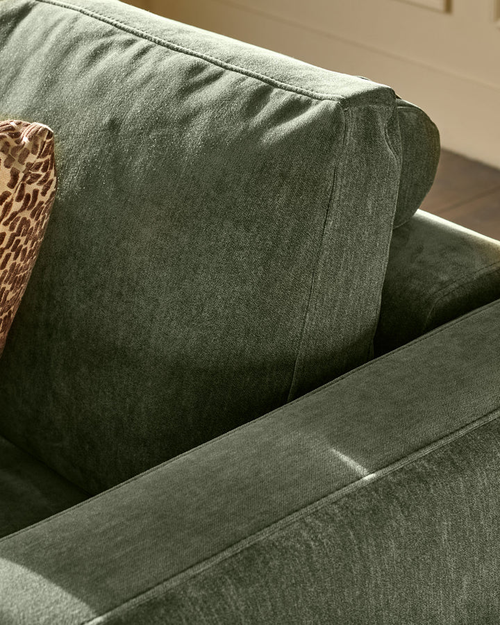 Eden 2-seater sofa in dark green fabric, close-up detail of cushioned backrest and armrest.