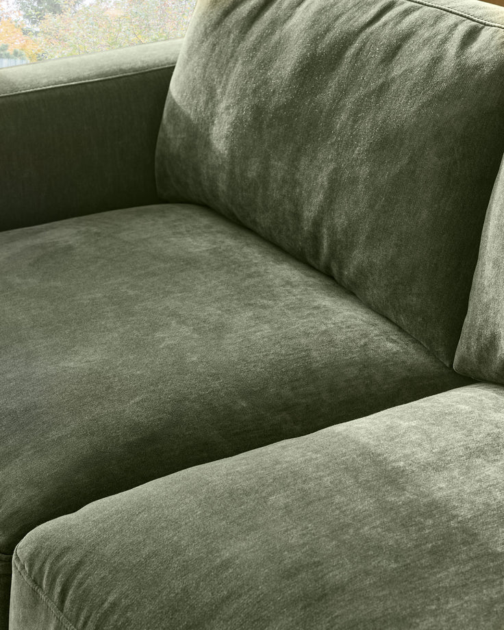 Eden 2-seater sofa in dark green fabric, close-up detail showing seat cushion and backrest with decorative pillow.