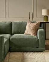 Dark green fabric right-facing small chaise sofa with cushioned seat and back, styled with a patterned pillow in a modern living room setting.
