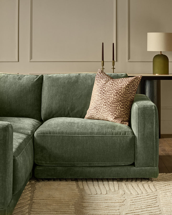 Dark green fabric right-facing small chaise sofa with cushioned seat and back, styled with a patterned pillow in a modern living room setting.