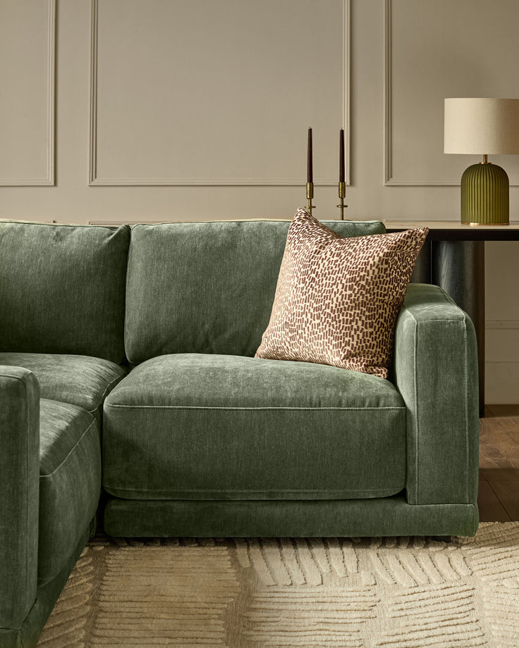 Dark green fabric right-facing small chaise sofa with cushioned seat and back, styled with a patterned pillow in a modern living room setting.