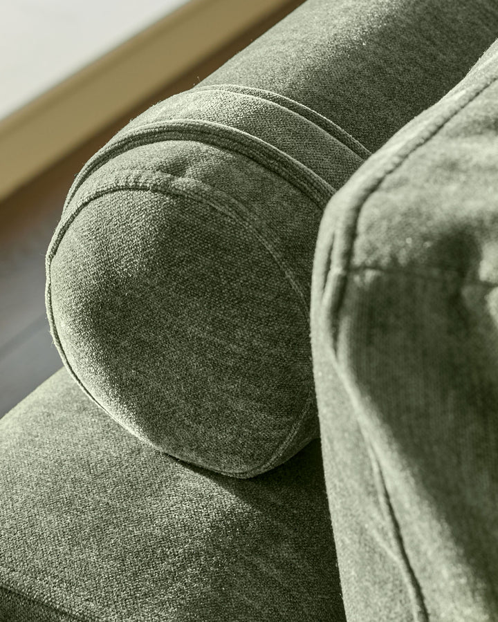 Dark green fabric 2-seater sofa, close-up detail of rounded arm and cushion texture.