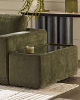 Dark green fabric side table with glass top and storage compartment, positioned next to matching armchair.