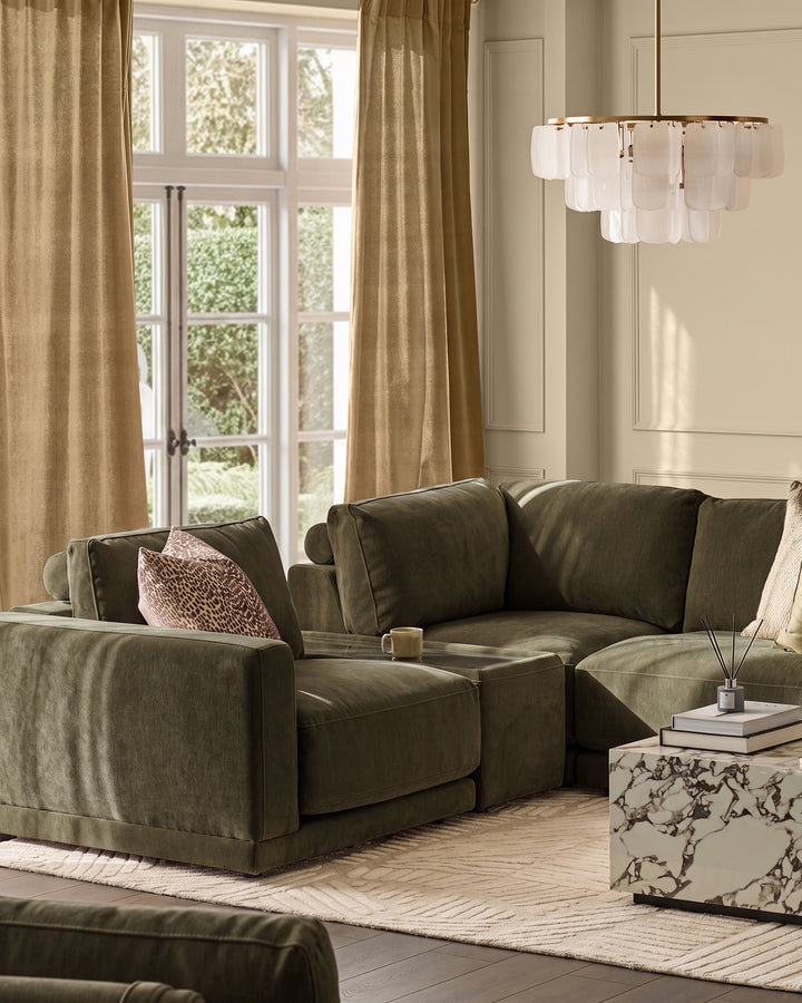 Dark green fabric modular sofa with cushioned seating and rolled arms in a bright living room setting.