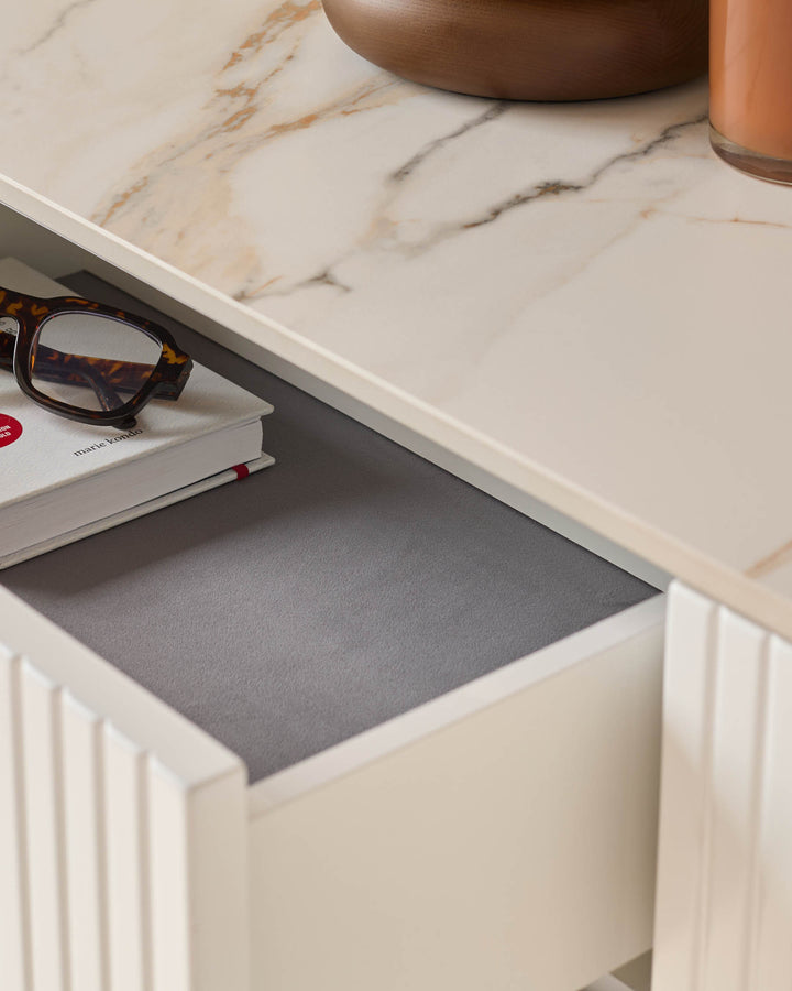 Edie Large Sideboard in natural ceramic with open drawer showing grey felt lining and tortoiseshell glasses on top.