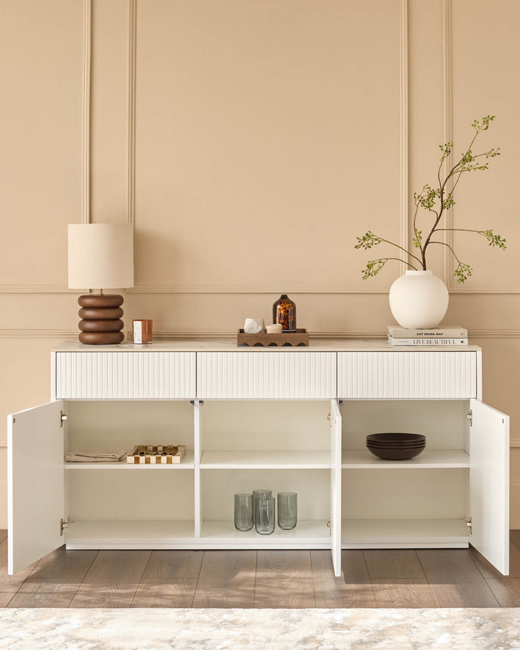 White large sideboard with vertical ribbed cabinet doors and open shelving, displayed with doors open showing interior storage and styled with decorative items.