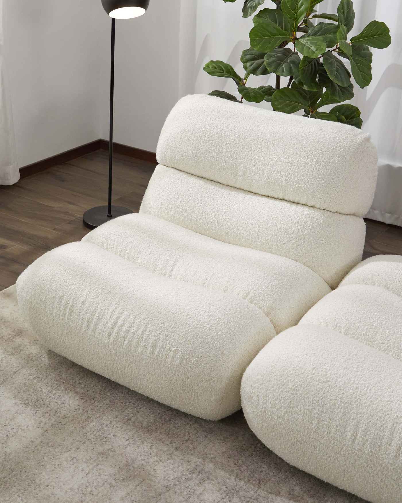 Plush, modern armchair with textured white fabric, featuring a unique contoured design with rounded cushions for the seat, back, and arms, presented in a cosy room setting with wood flooring and neutral decor.