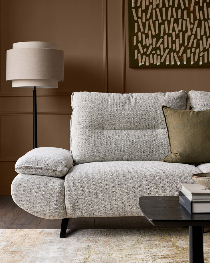 Elio 3-seater sofa in grey fabric with curved arms, angled legs, and decorative cushions in a styled living room setting.