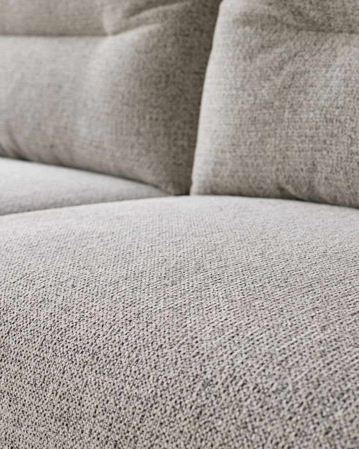 Close-up of grey fabric texture on Elio 3-seater sofa seat and cushions, showing woven upholstery detail.