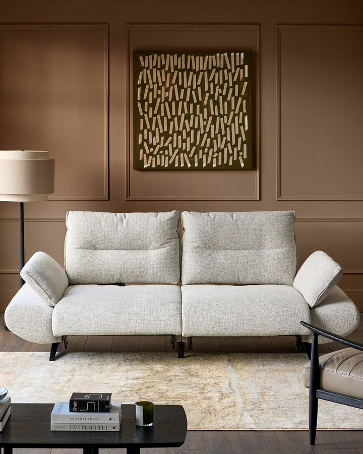 Elio 3-seater sofa in grey fabric with curved armrests and black metal legs, displayed in a styled living room setting.