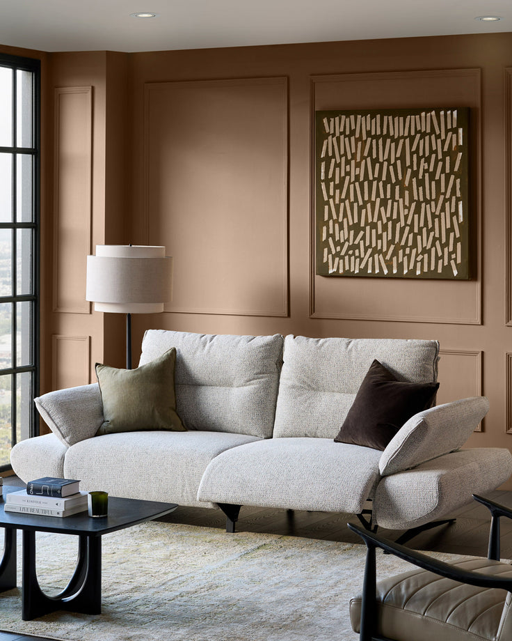 Elio 3-seater sofa in grey fabric with curved arms, displayed in a warm brown living room with decorative pillows.
