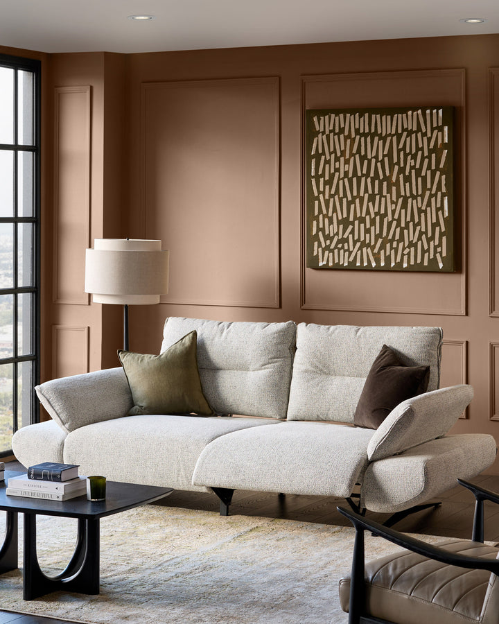 Elio 3-seater sofa in grey fabric with curved arms and black metal legs, displayed in a warm brown living room setting.