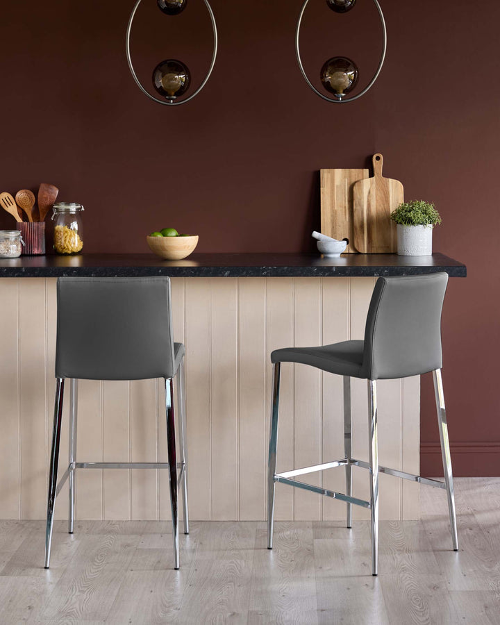Two grey bar stools with chrome legs sit at a kitchen island with a black worktop and wooden base.