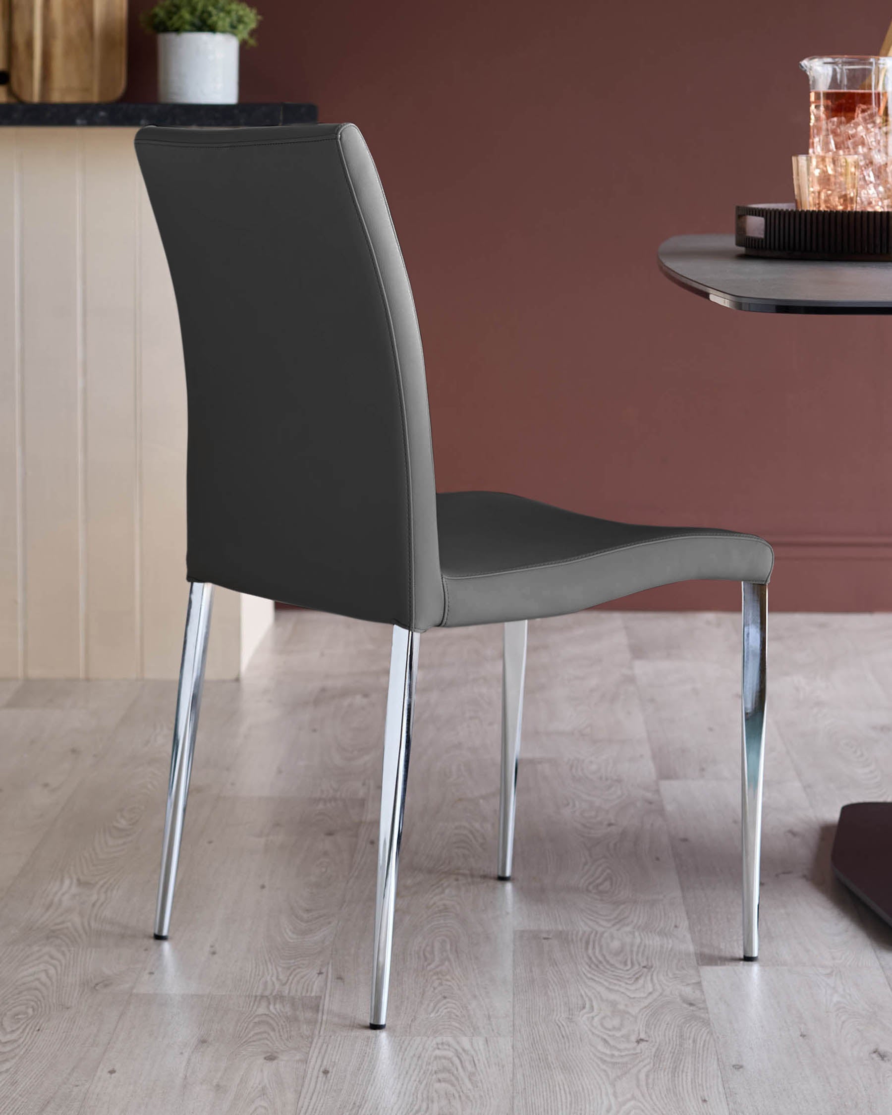 A grey chair with chrome legs is in front of a table. The background features wooden wall panels and a brown wall.