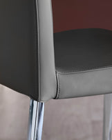 Close-up of a grey leather chair with chrome legs, showcasing its modern design and quality craftsmanship.