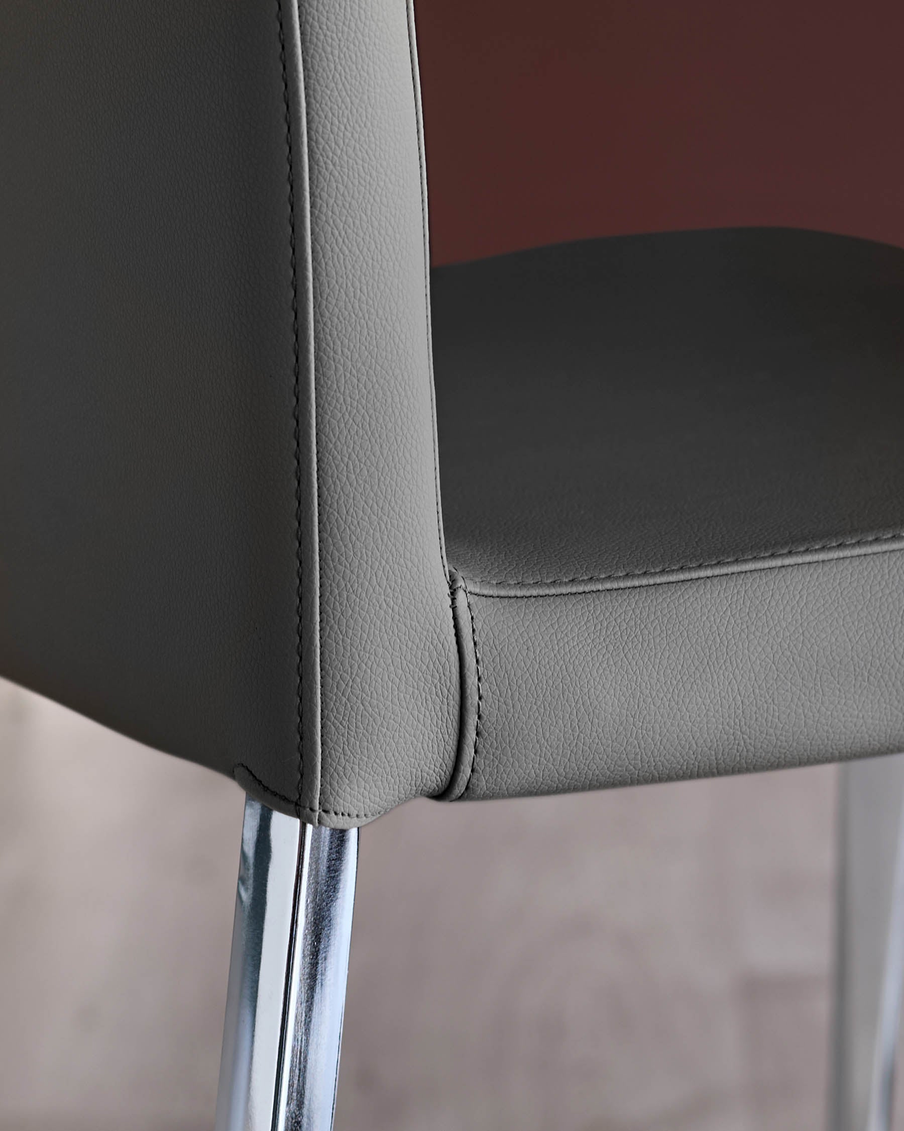 Close-up of a grey leather chair with chrome legs, showcasing its modern design and quality craftsmanship.