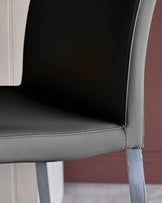 Close-up of a grey leather chair with a sleek chrome leg. Focus on the seat and back detail.