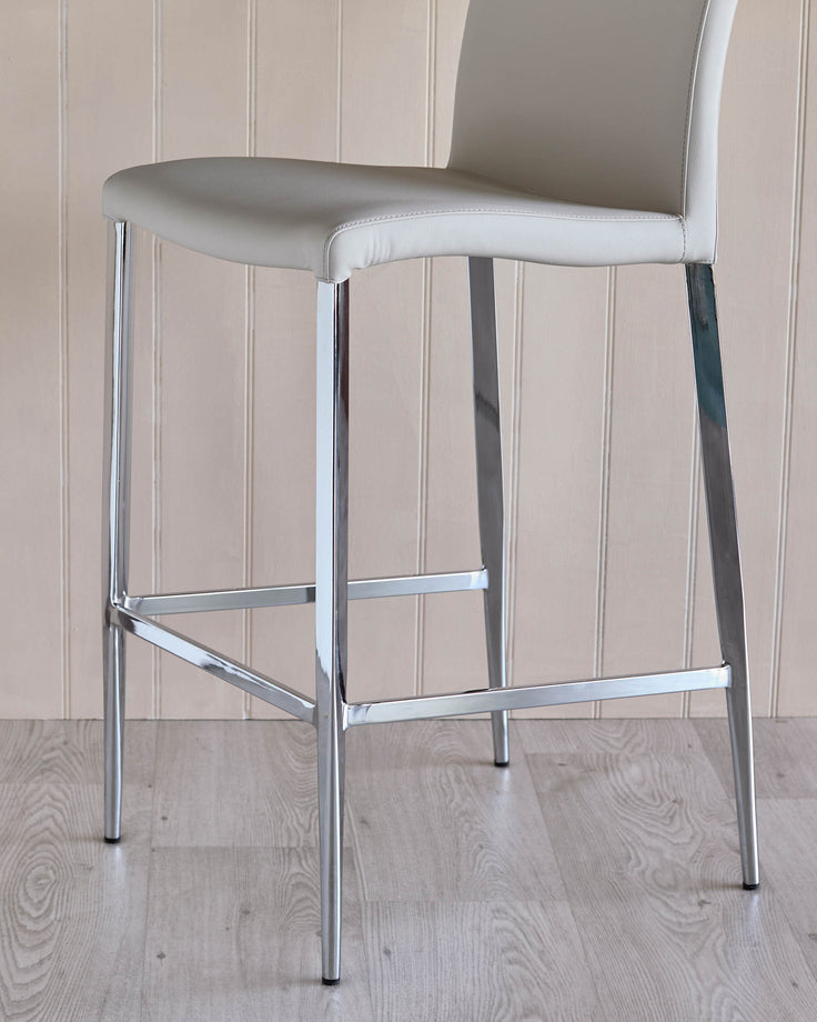 A chrome stool with a padded cream seat against a panelled wall and light wood floor.