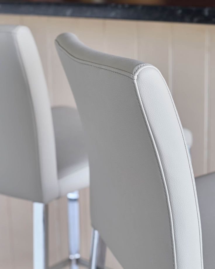 Close-up of two stylish, light grey bar stools with chrome legs. Perfect for a modern kitchen or bar area.