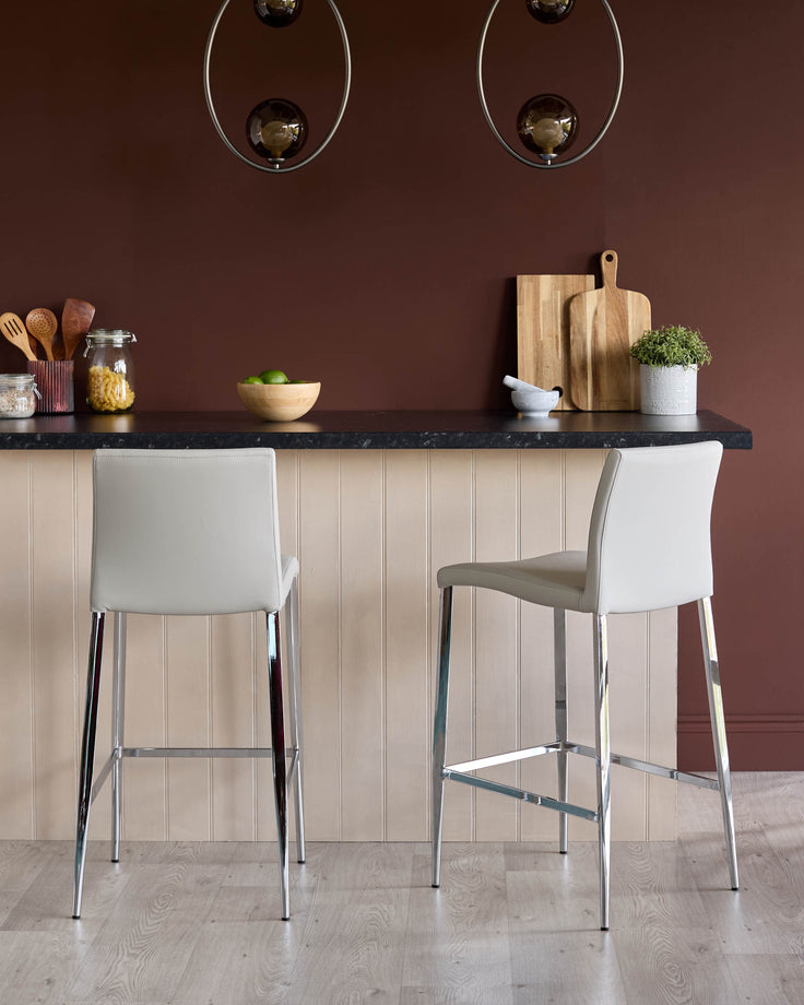 Elise faux leather bar stool in light grey with chrome legs, shown as a pair at a black countertop in a modern kitchen setting.